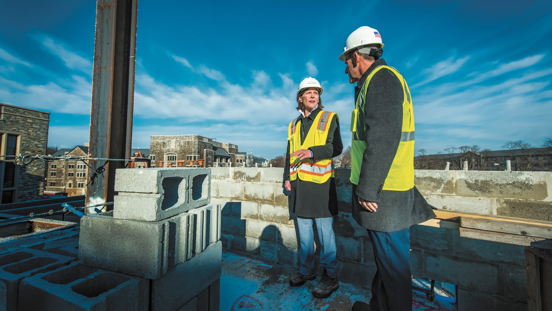 Marilou Smith and Robert Morro atop the Villanova Performing Arts Center building wearing hard hats and safety vests