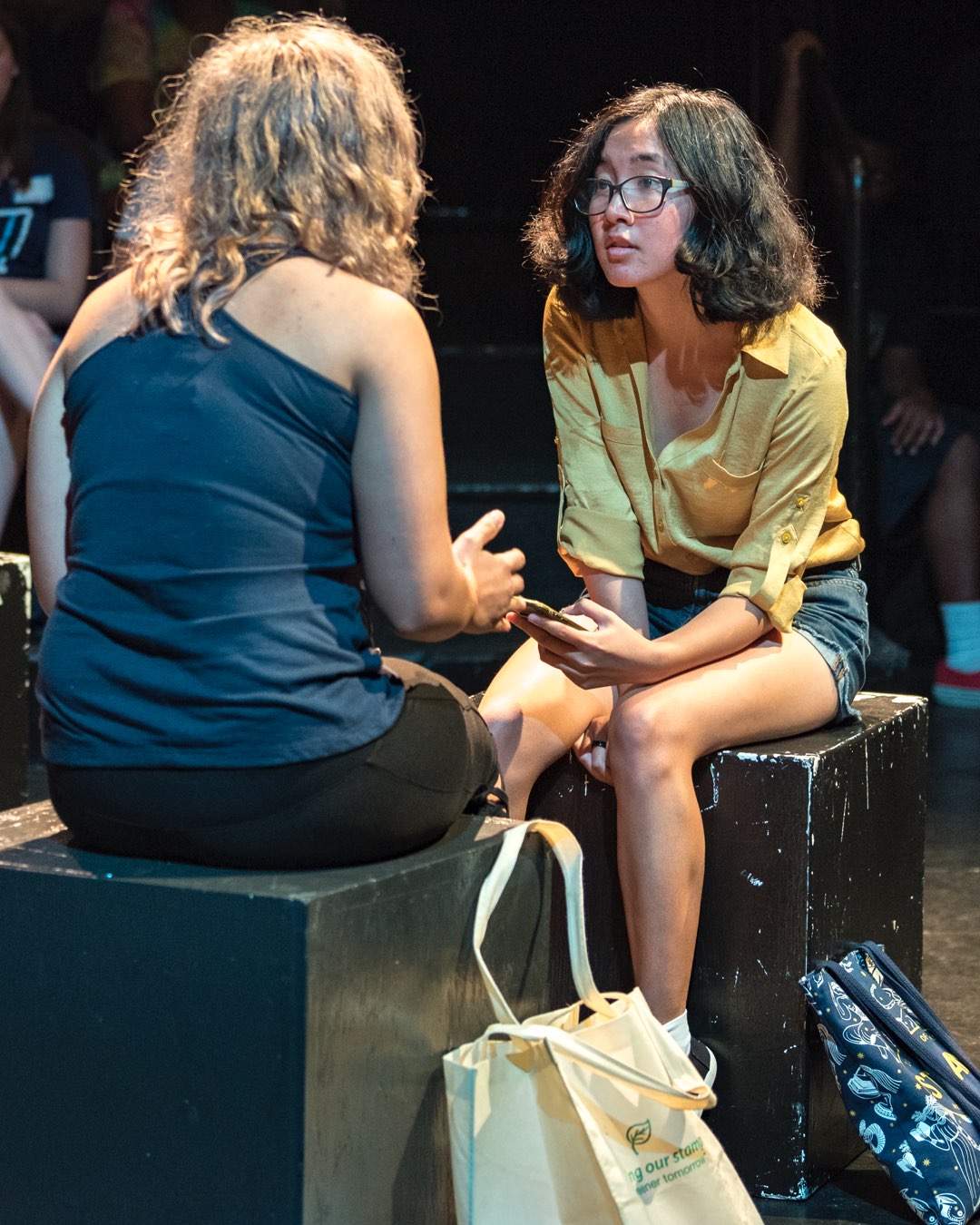 A male and female student seated and a standing male student in Vasey Theatre all looking at a phone
