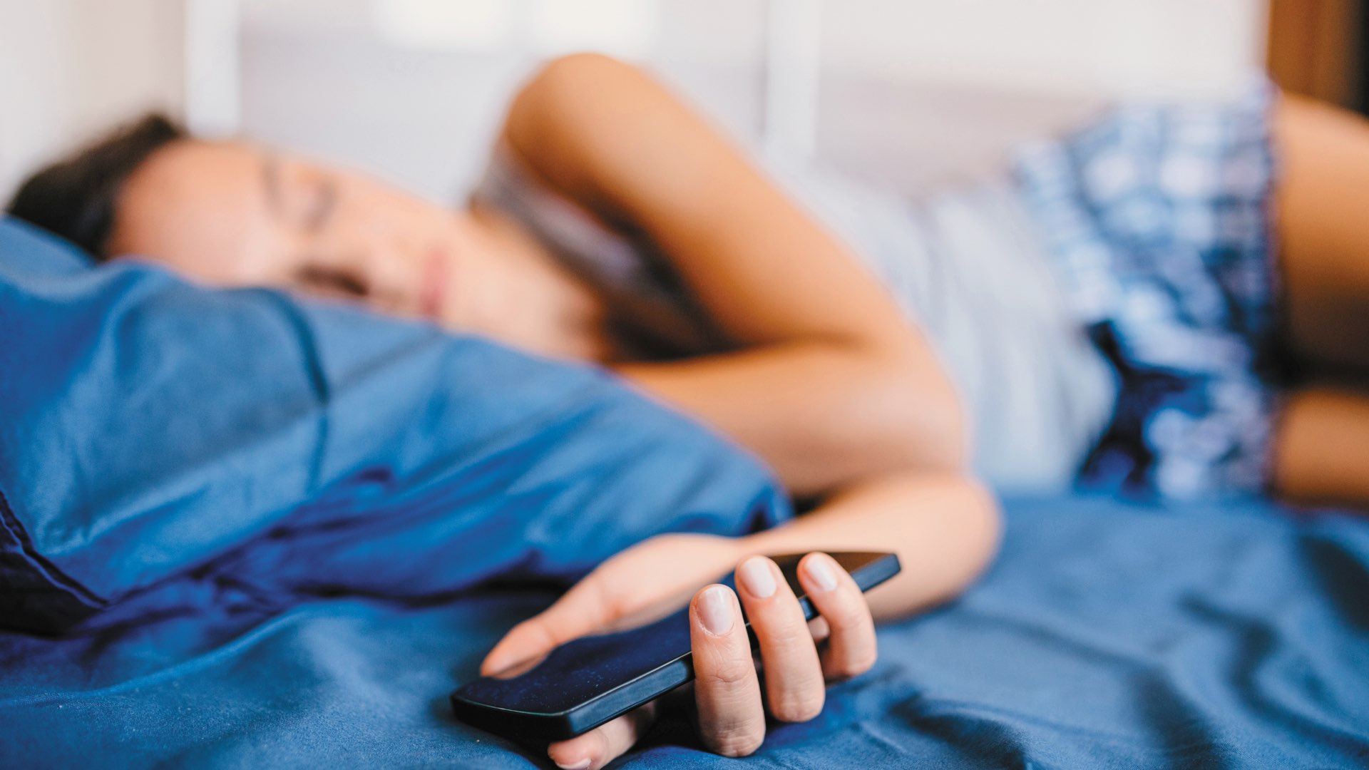A young female sleeping in bed with a phone in her hand
