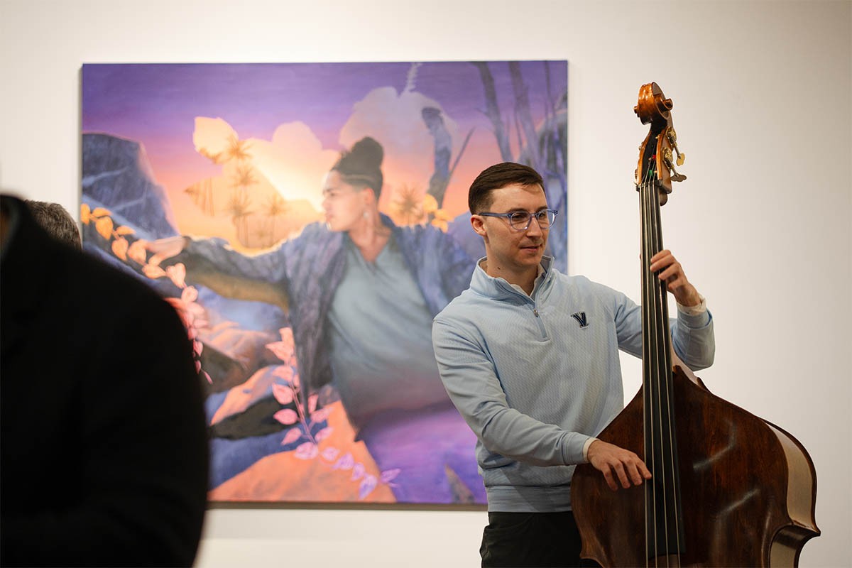 Individual playing the chello at an art exhibit with a painting in the background