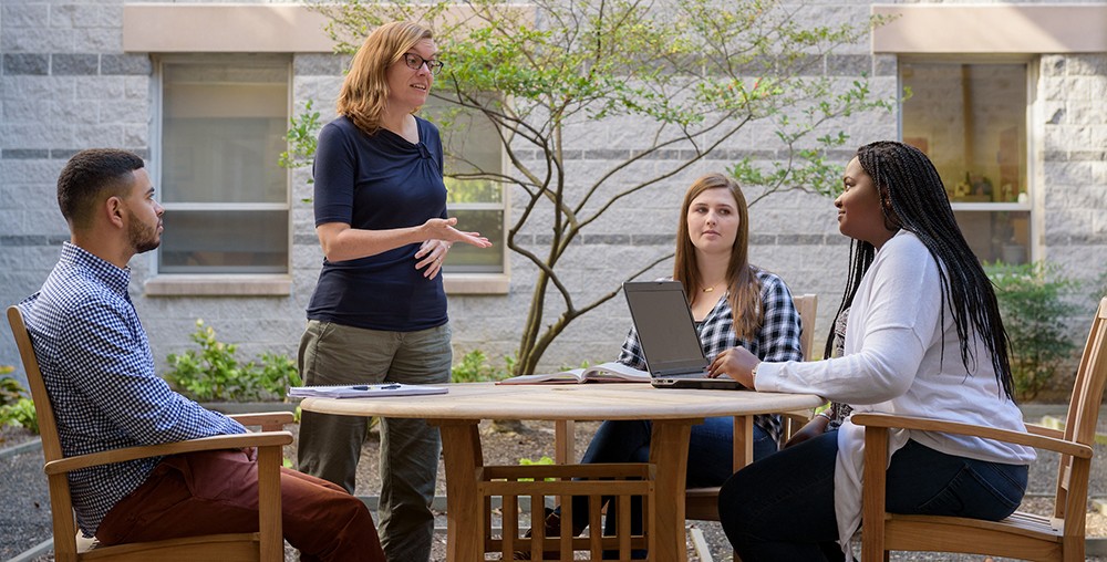 Faculty member talking with graduate students seated at an outdoor table. Faculty member talking with graduate students seated at an outdoor table.