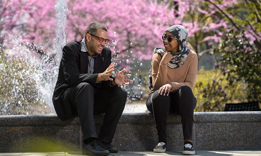 Theology discussion Theology professor talking to a student in front of a fountain on a spring day