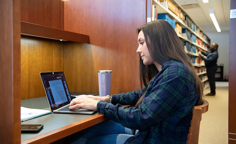 A student works at her computer in the library. A student works at her computer in the library.