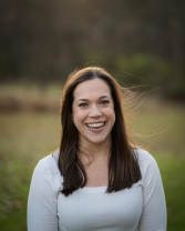 Woman with brown hair standing in field smiling