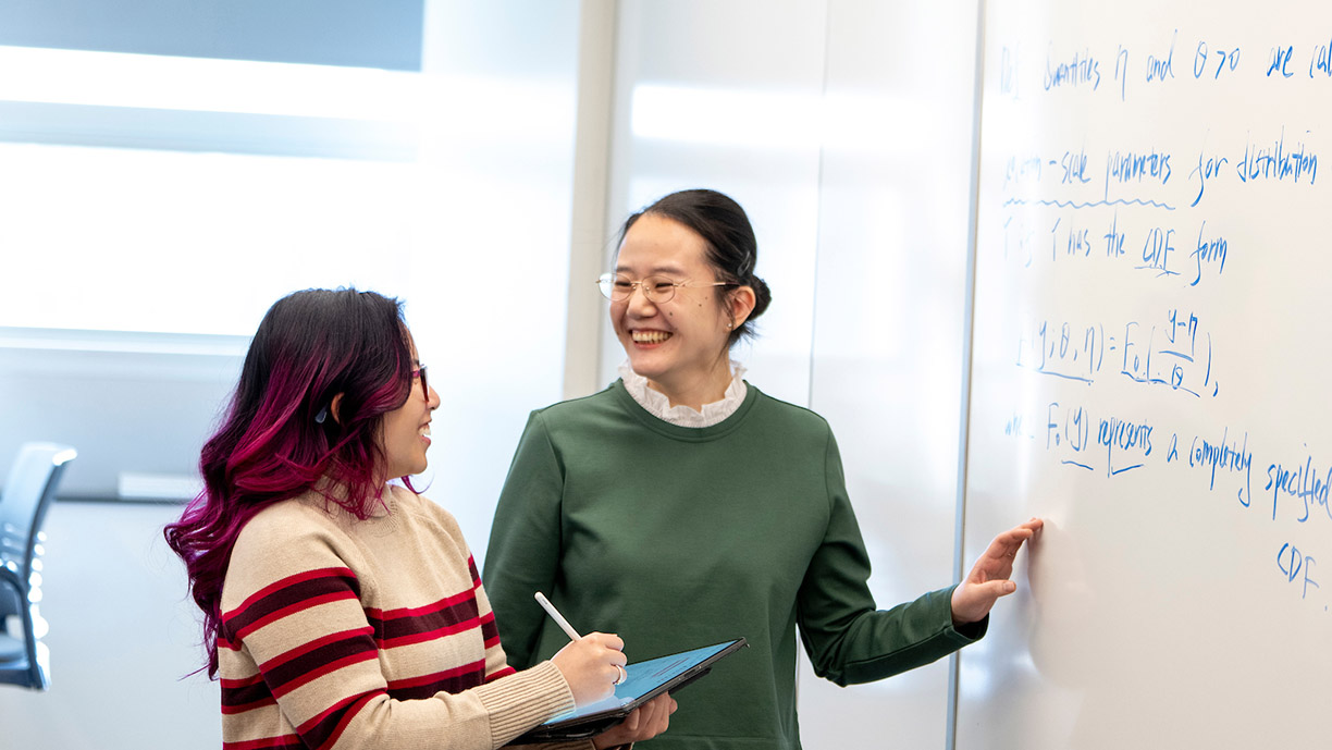 faculty standing and talking to a student at a whiteboard